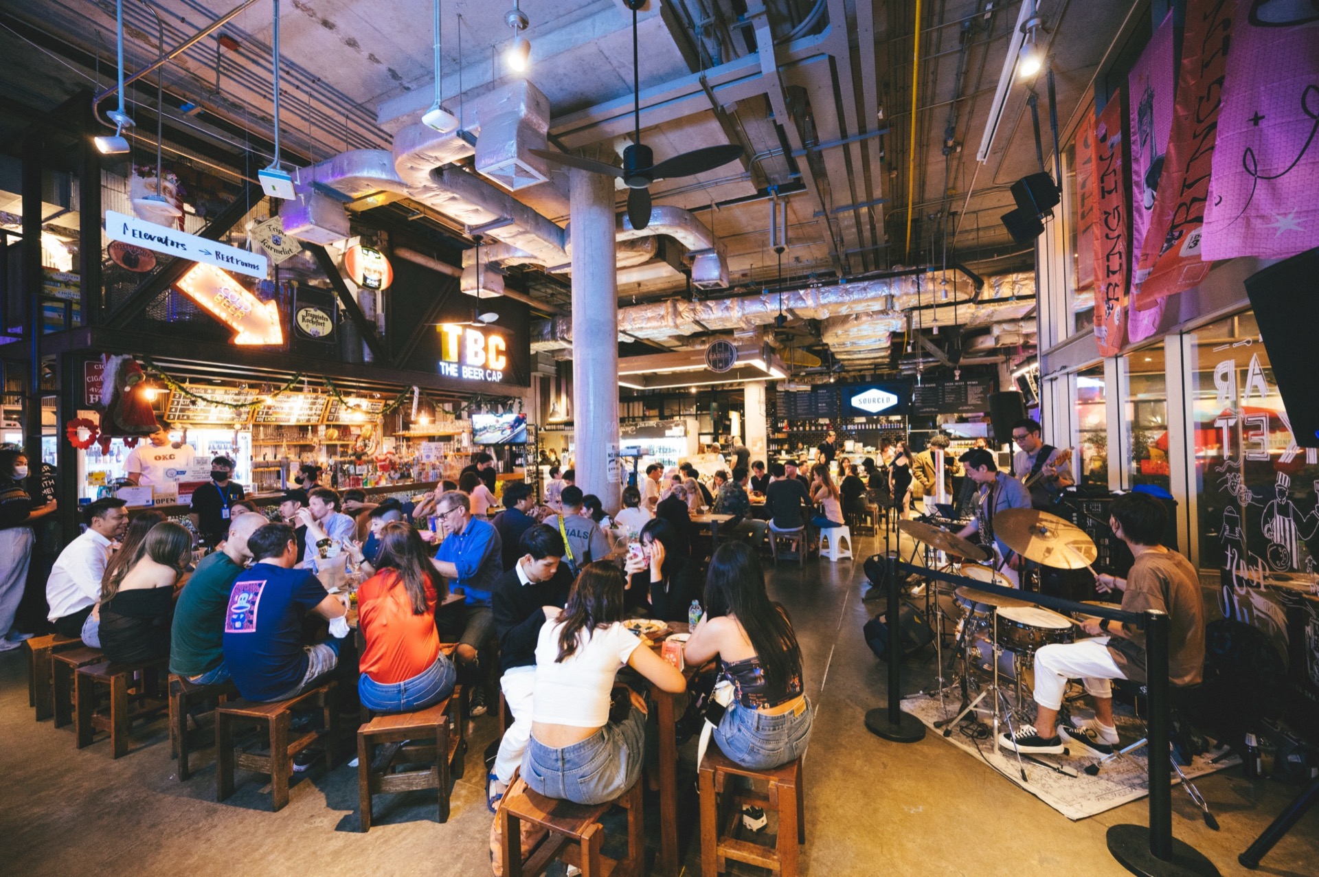The Beer Cap でのバンドのライブ演奏。背後にバーカウンターと TBC の看板